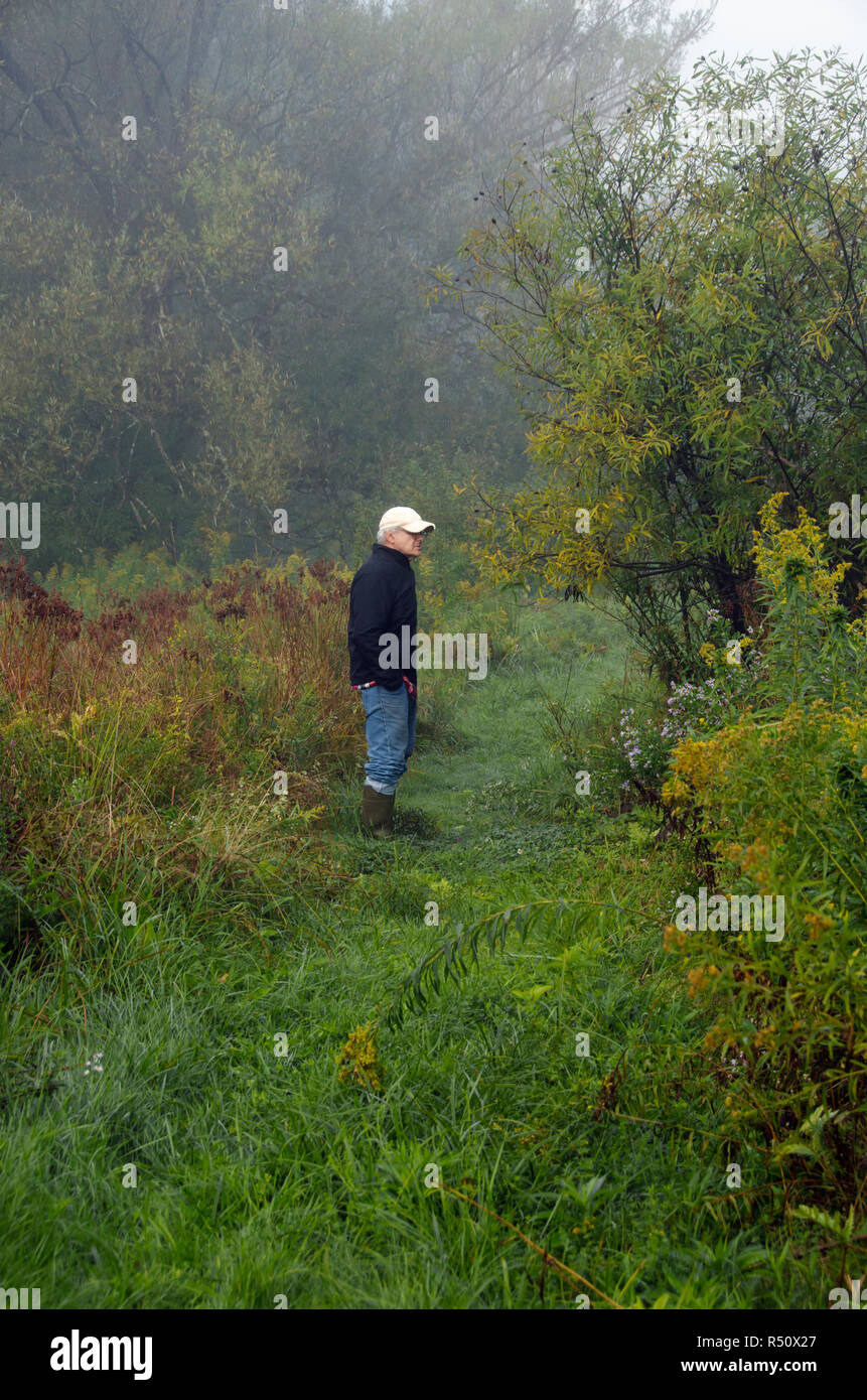 Un senior uomo in piedi da solo tra il fogliame di autunno Foto Stock