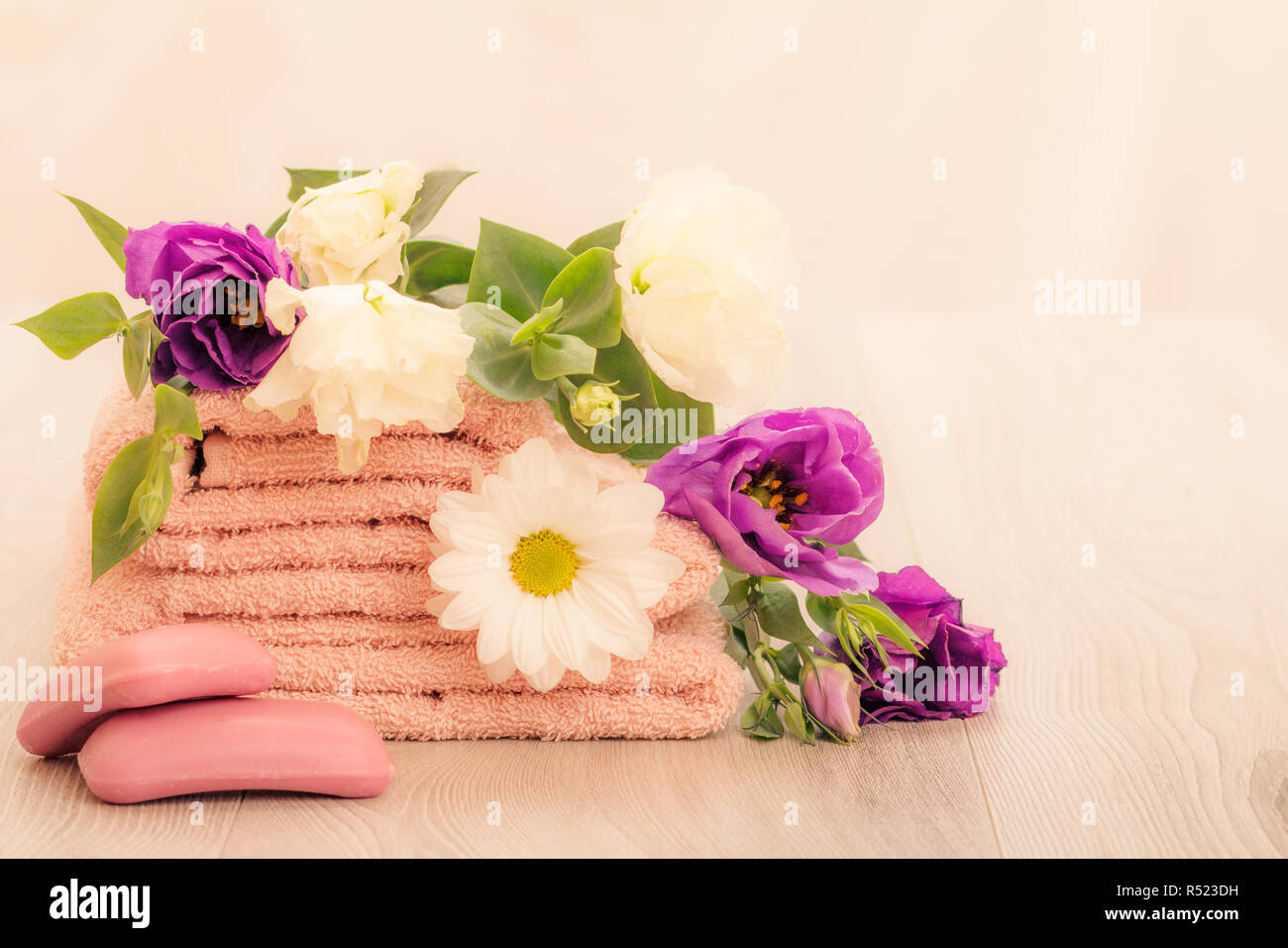 Pila di soffici asciugamani di spugna con bianco e fiori viola, sapone su sfondo rosa. I prodotti spa. Foto Stock