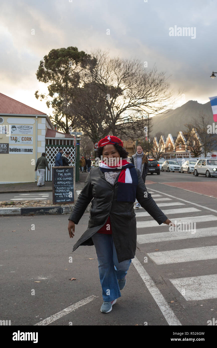 Donna che indossa rosso francese berretto e sciarpa in bandiera francese colori attraversando la strada in inverno usura durante la festa della bastiglia in Franschhoek Foto Stock