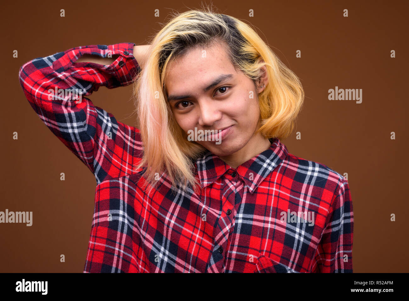Giovane uomo asiatico indossando abiti eleganti contro sfondo marrone Foto Stock