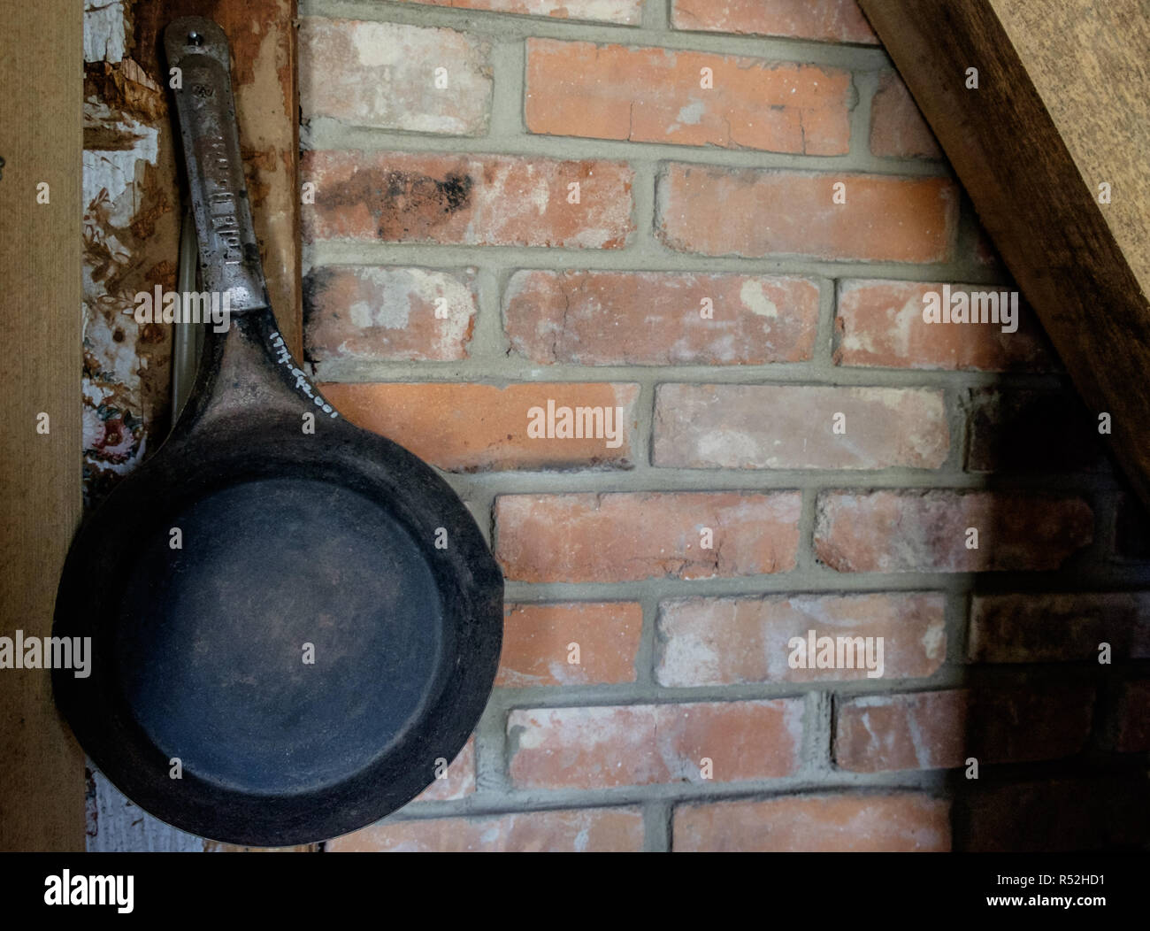 Vintage padella in ghisa consegnando il vecchio muro in mattoni con travi di legno in angolo. Interno di una casa, piazza di castagno villaggio storico, McKinney, Texas Foto Stock