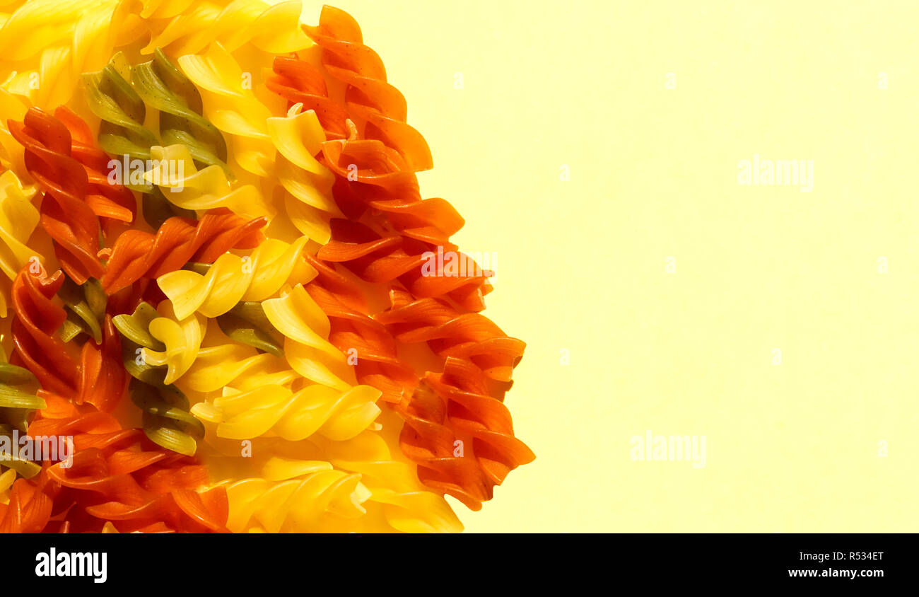 Multicolore pasta grezza di close-up di luce su sfondo giallo. Vista dall'alto. Abstract background alimentare, copia dello spazio per il testo Foto Stock