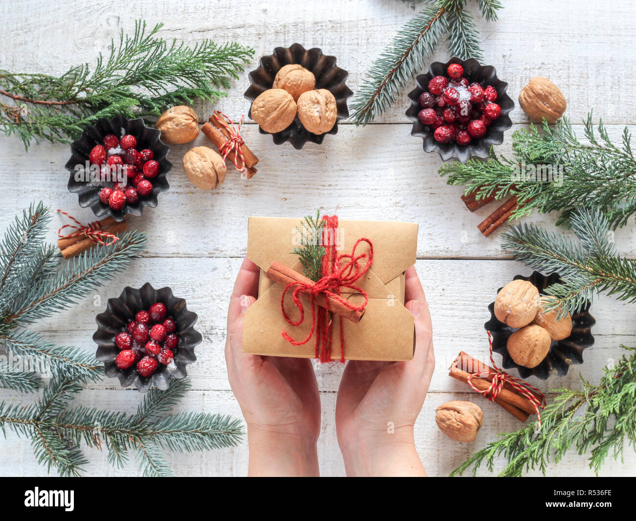 Umore natalizio piatto composizione laici con bacche rosse, dadi e bastoncini di cannella su un di legno bianco e di sfondo presente nelle mani Foto Stock