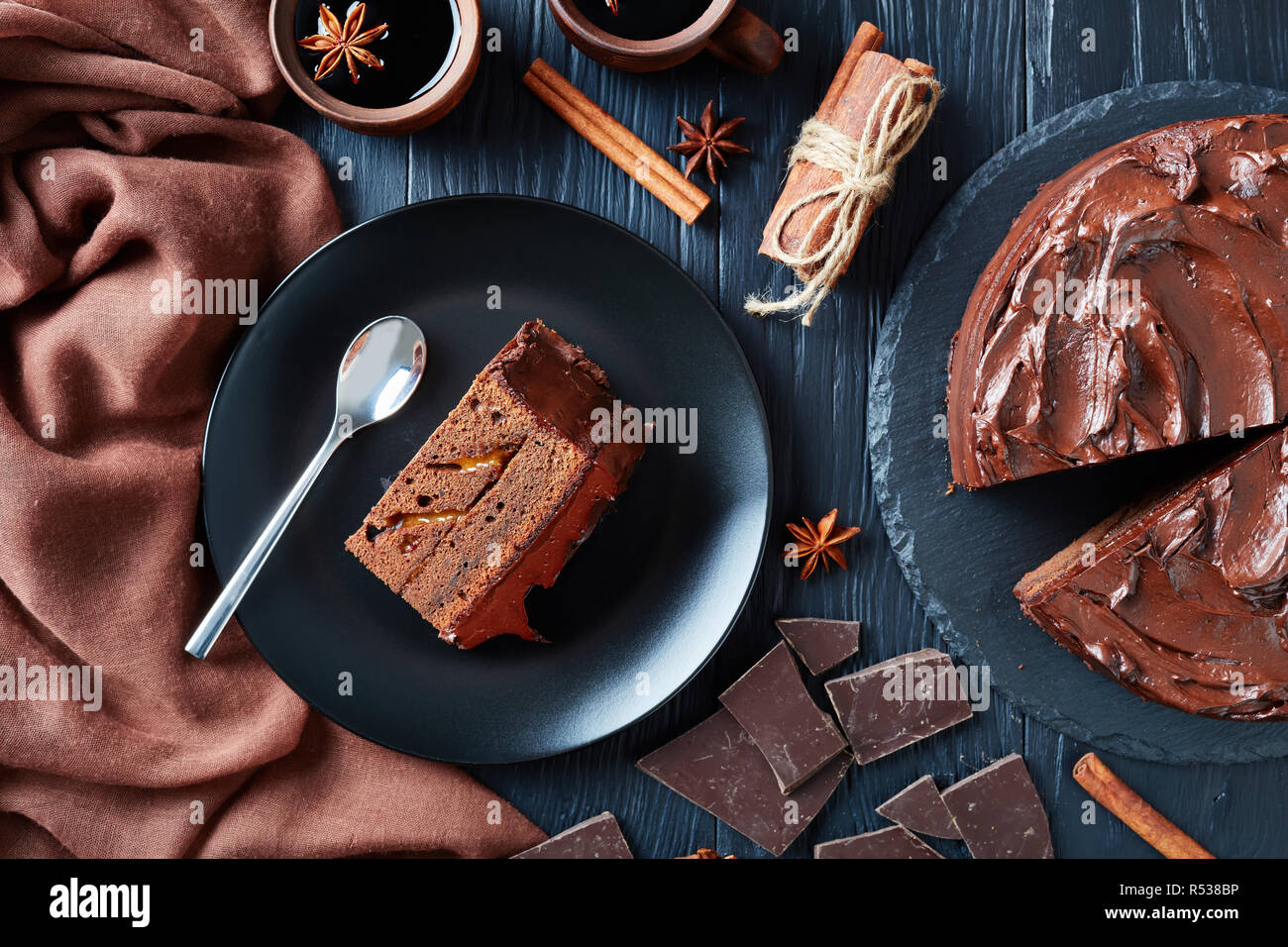 Porzione di torta al cioccolato con marmellata di albicocche il riempimento e rabboccato con glassa al cioccolato servito su una piastra nera con vin brulé in argilla tazze rustico su un bla Foto Stock
