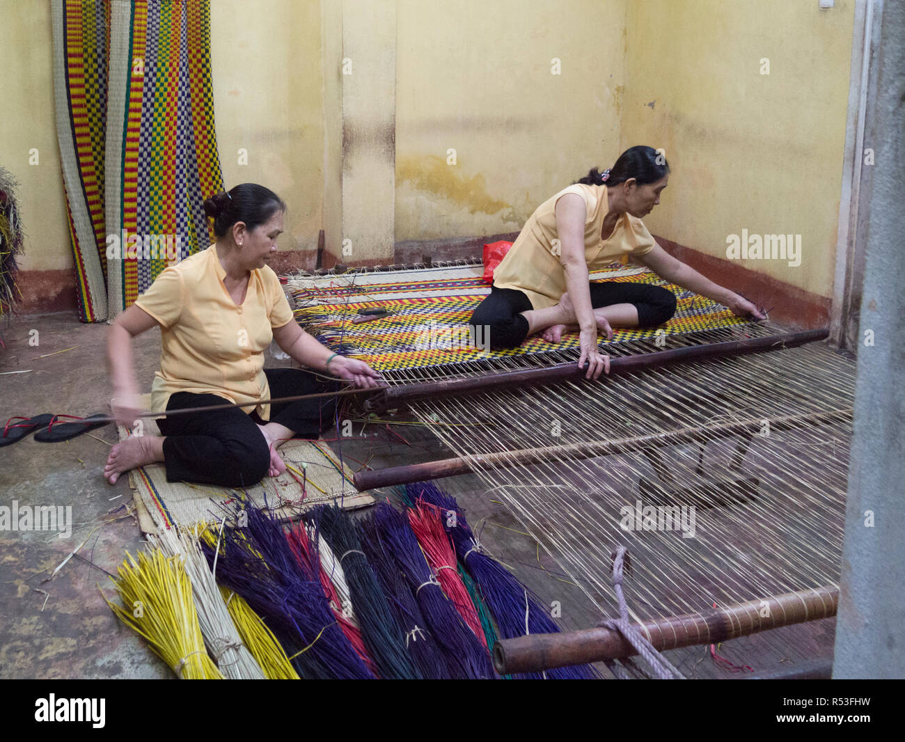 Due donne vietnamita seduta sul pavimento della seta negozio di vendita la tessitura tappeti colorati Hoi An Vietnam Asia Foto Stock