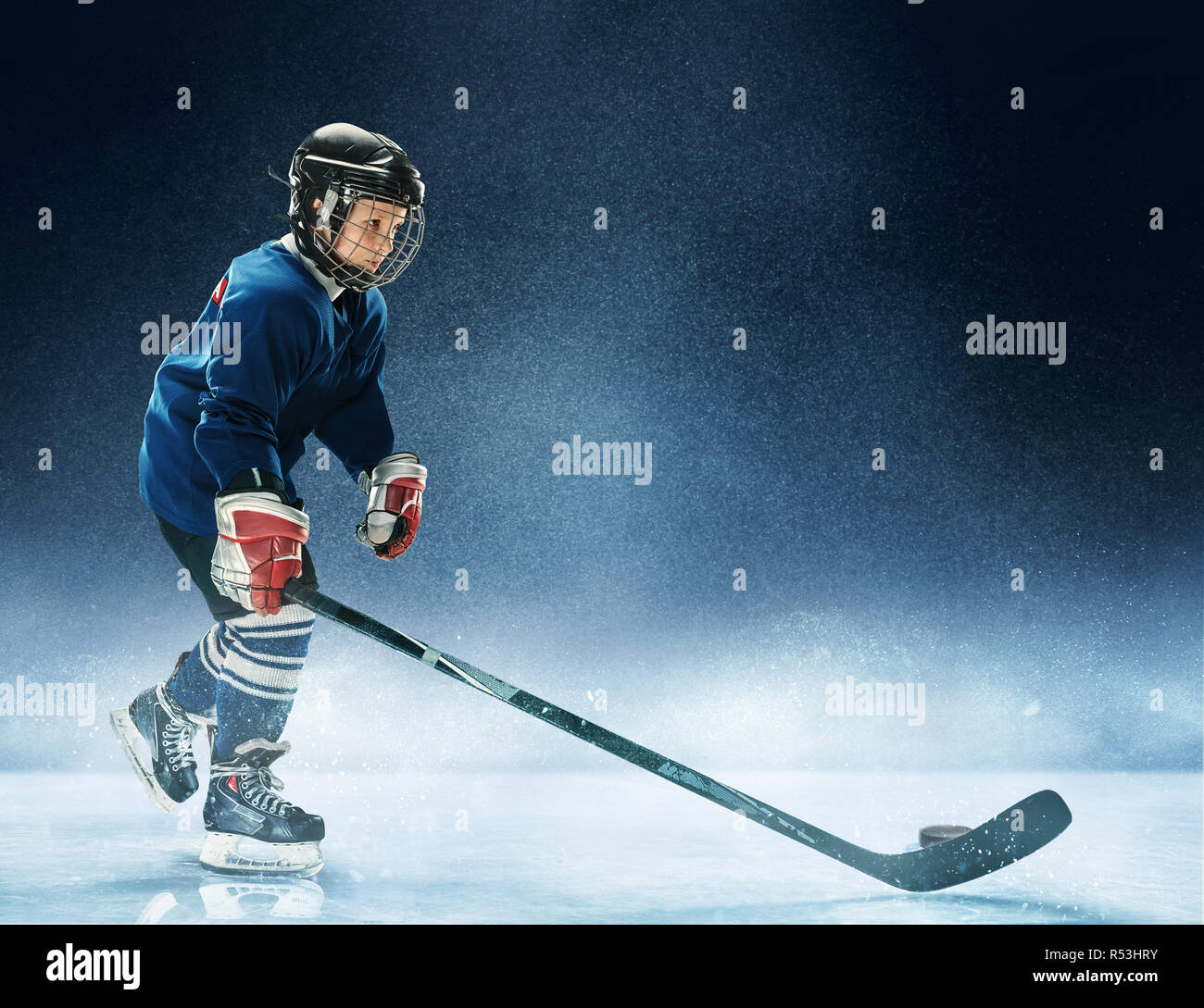 Little Boy riproduzione di hockey su ghiaccio all'arena. Un giocatore di hockey in uniforme con le apparecchiature sopra uno sfondo blu. L'atleta, bambino, sport, il concetto di azione Foto Stock