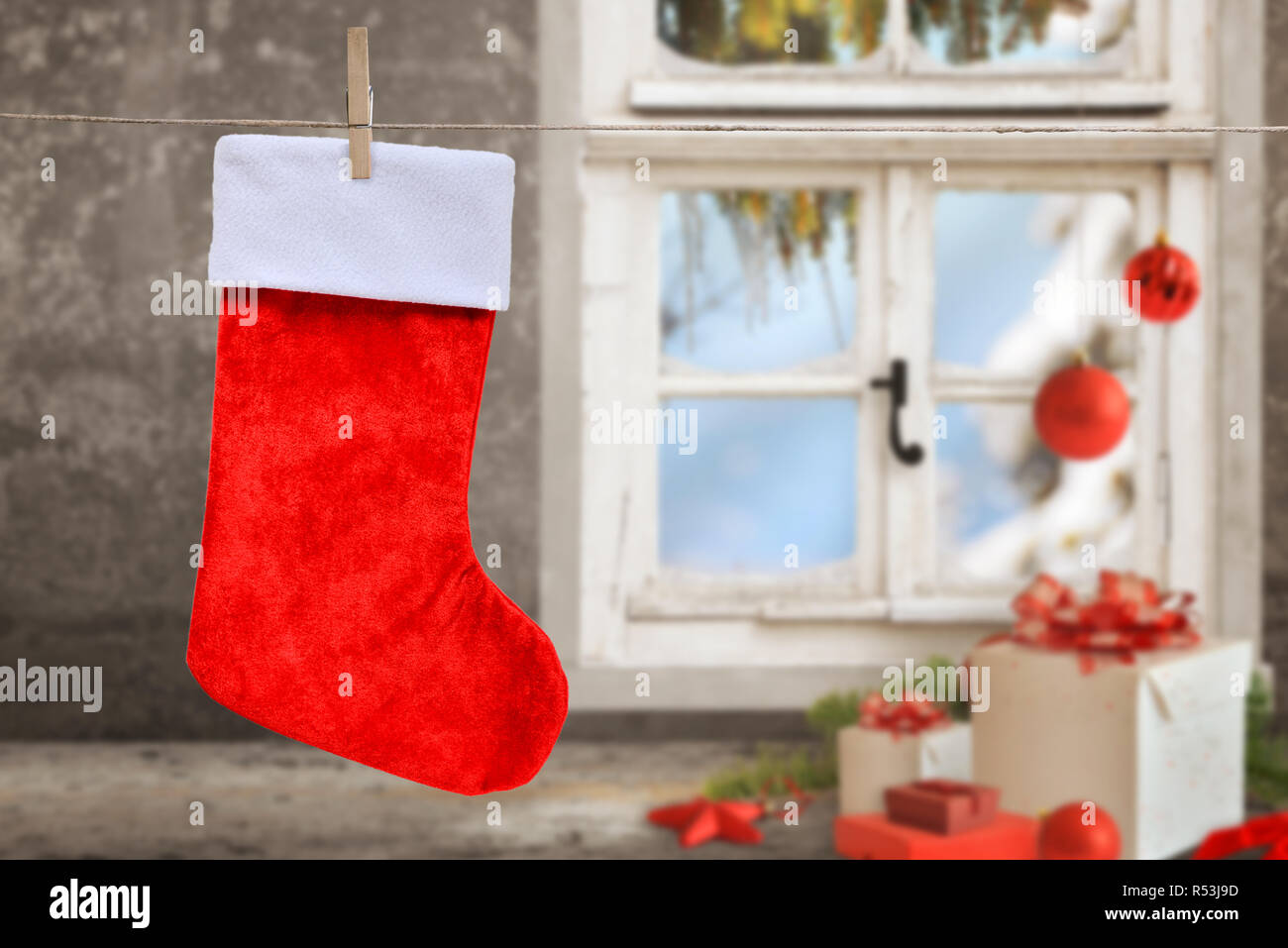 Vuoto calza di Natale appeso a una fune. Pulire il calzino per mockup, testo di saluto. Regali di natale, palline, decorazioni e la finestra in background. Foto Stock