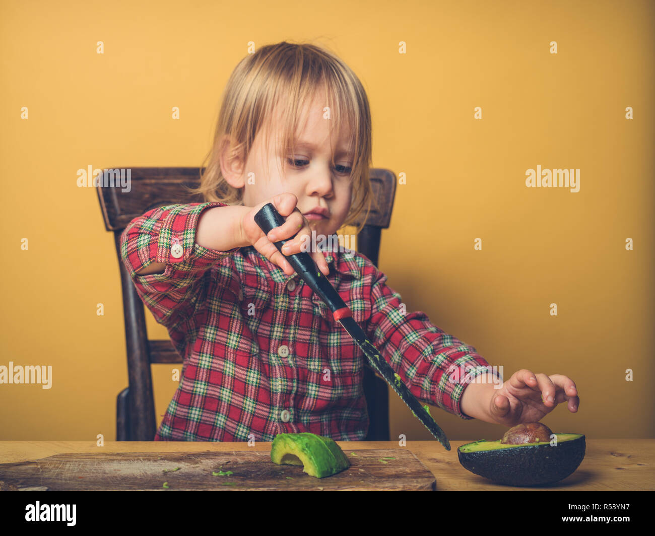 Un po' di toddler boy è il taglio di avocado al tavolo Foto Stock