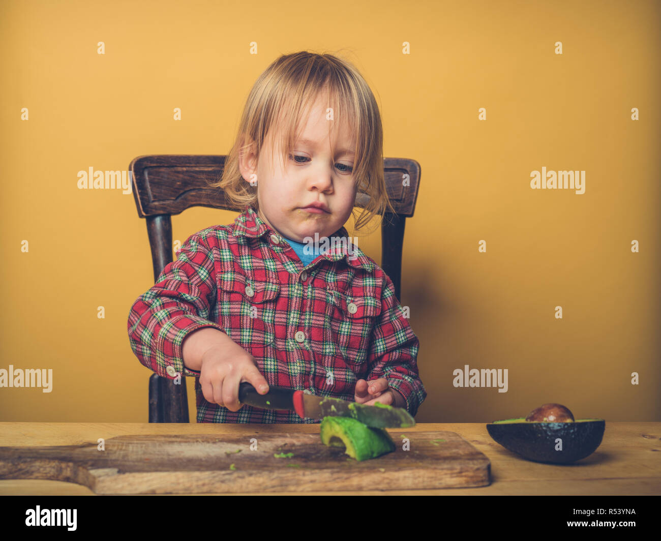 Un po' di toddler boy è il taglio di avocado al tavolo Foto Stock