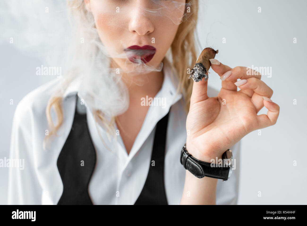 Vista ritagliata della moda ragazza bionda di fumare il sigaro su grigio Foto Stock