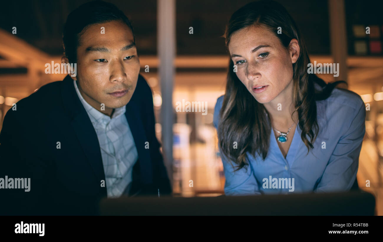 Partner commerciali multietnici che lavorano fino a tarda notte in ufficio. colleghi d'affari seduti insieme a guardare un notebook che lavora a tarda notte Foto Stock