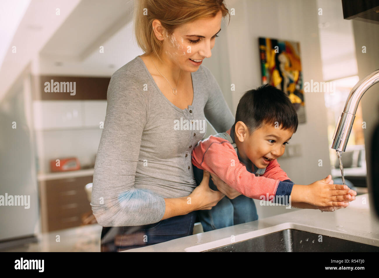 Donna aiutando ragazzino di lavarsi le mani dopo la cottura. Figlio di lavare le mani con la madre tenendo lui al lavello. Foto Stock