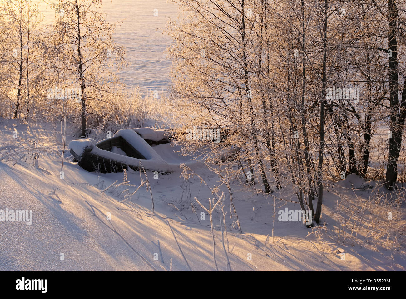 Inverno landsgape con la barca di legno sotto la neve nella luce calda del sole con copyspace per testo Foto Stock