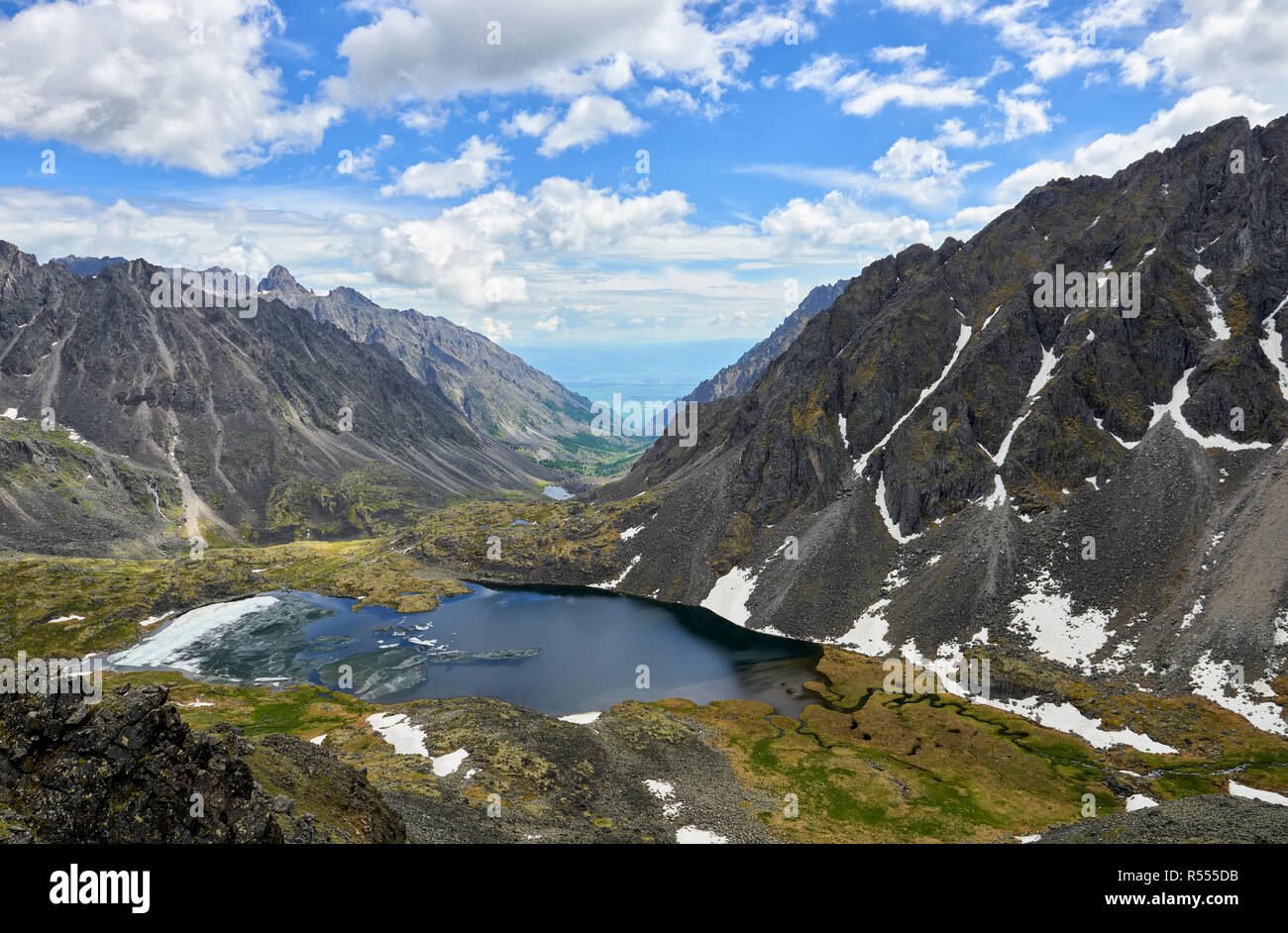 Lago di montagna con ghiaccio galleggiante nella stretta valle racchiusa da montagne. Vista dall'altezza del picco. Eastern Sayan. Asia centrale Foto Stock