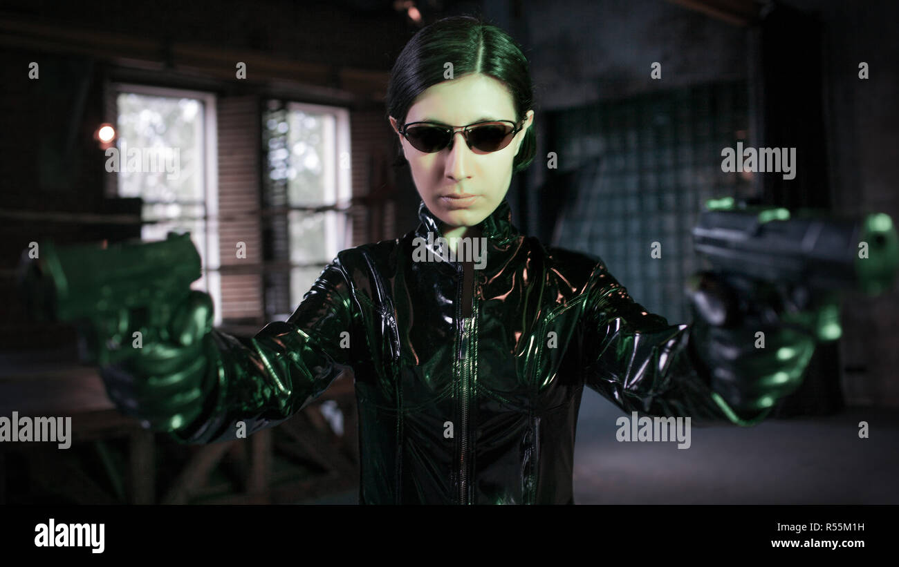 Virus e sicurezza informatica, concetto. giovane donna vestita in stile Matrix. Ragazza hacker in cuoio nero con le pistole. Foto Stock
