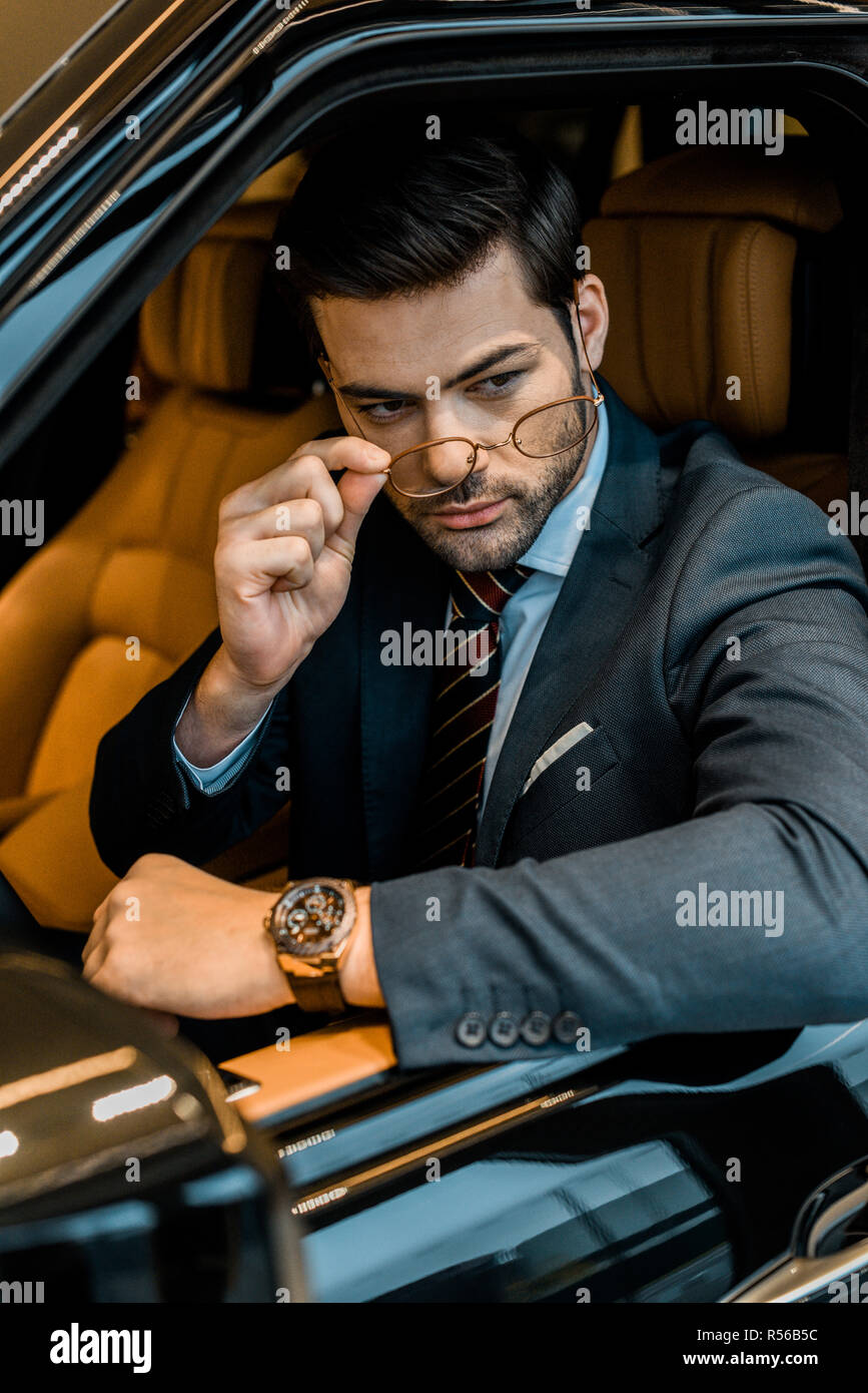 Elegante imprenditore con orologio di lusso di mettere su un occhiale seduti in auto Foto Stock