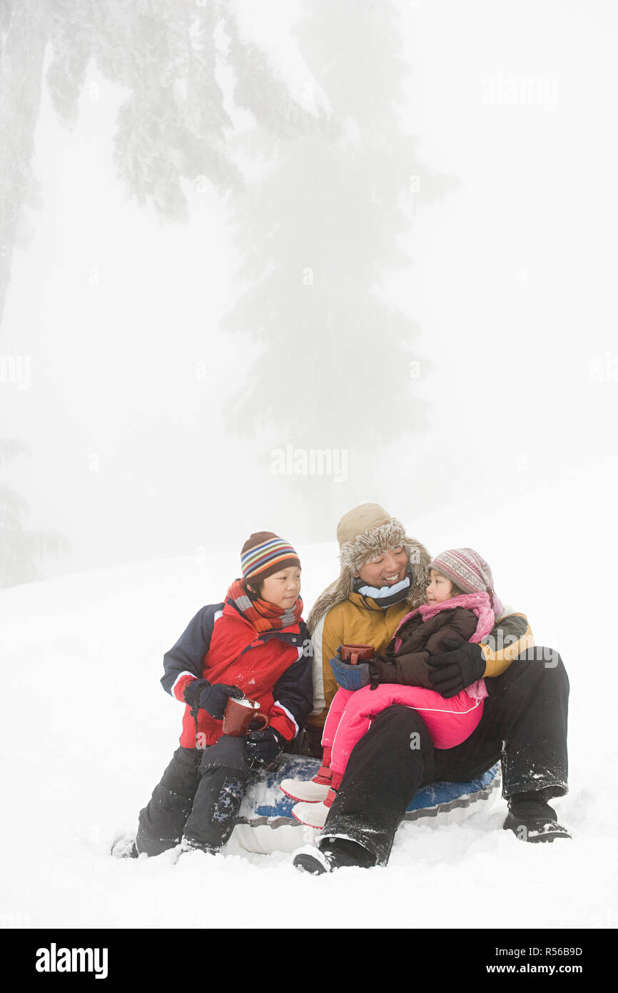 Padre e figli aventi bevanda calda nella neve Foto Stock