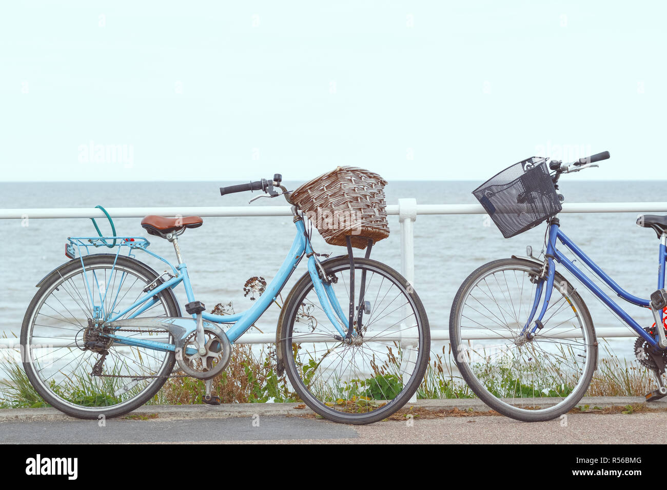 Due biciclette con ceste incatenato al recinto della promenade di Southwold, REGNO UNITO Foto Stock