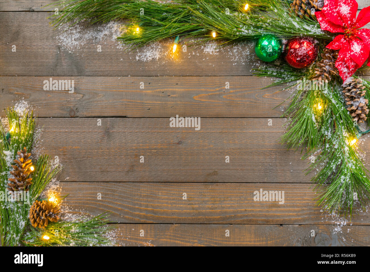Sfondo di natale con neve, abete rosso verdi, ornamenti e luci su weathered tavole di pino Foto Stock