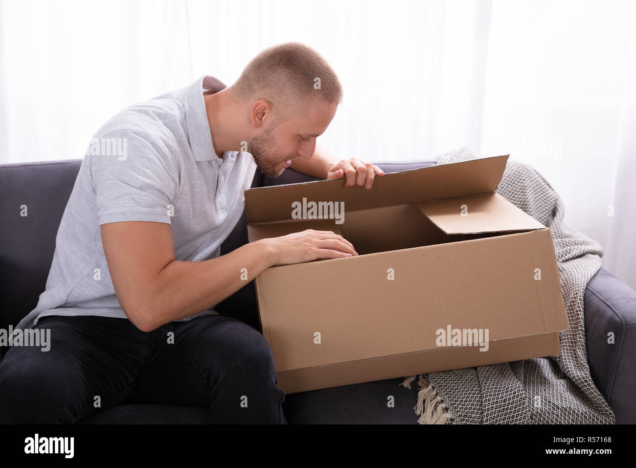 Giovane uomo seduto sul divano guardando all'interno consegnato il pacco Foto Stock