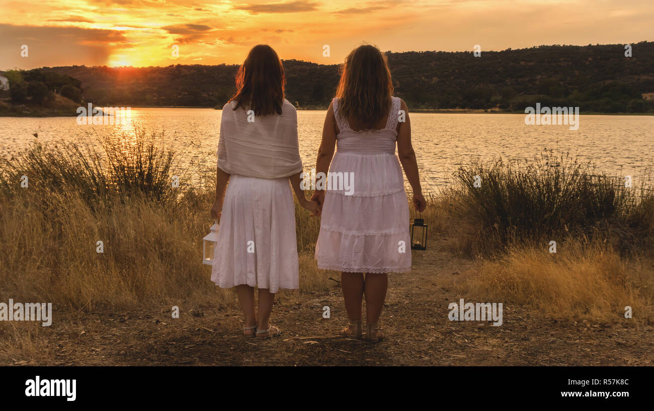 Due donne a guardare il tramonto con abito bianco e lanterna sulle loro spalle Foto Stock