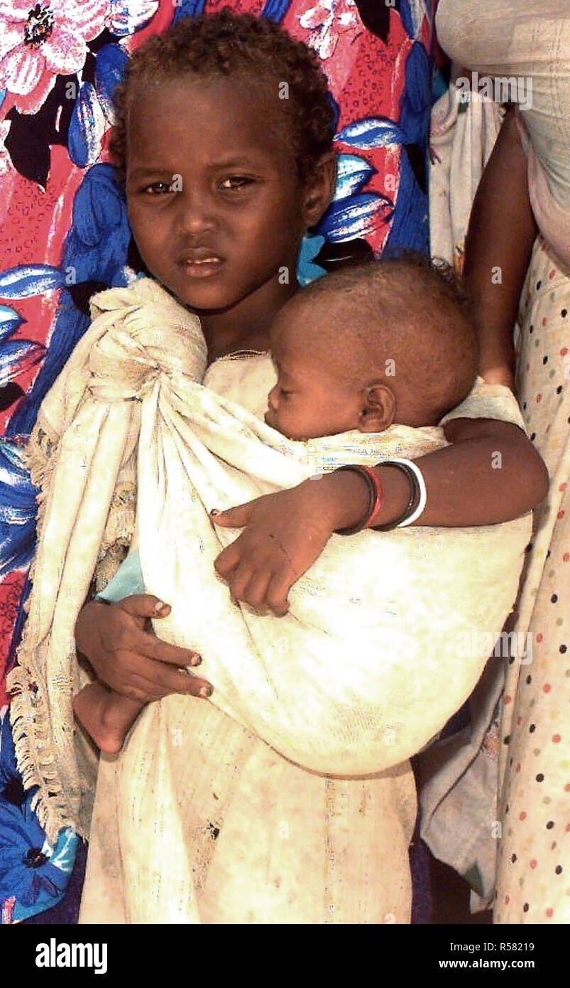 1993 - dritto, medium close-up di una giovane ragazza somala cullano la sorella in fascia che è legato sulla sua spalla. Essi sono in attesa in linea per vedere US Navy medici conducendo un medico civile Programma d'azione nella capitale Mogadiscio, Somalia. Foto Stock