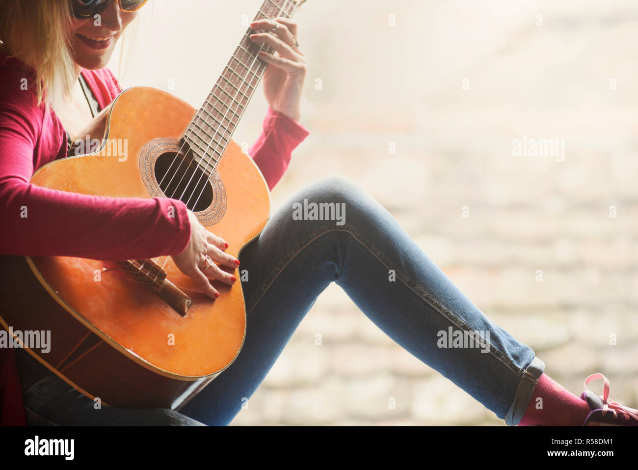 Primo piano di giovani felici hipster donna suona la chitarra con copyspace sfondo. Divertimento estivo e lo stile di vita della gioventù concetto. Foto Stock