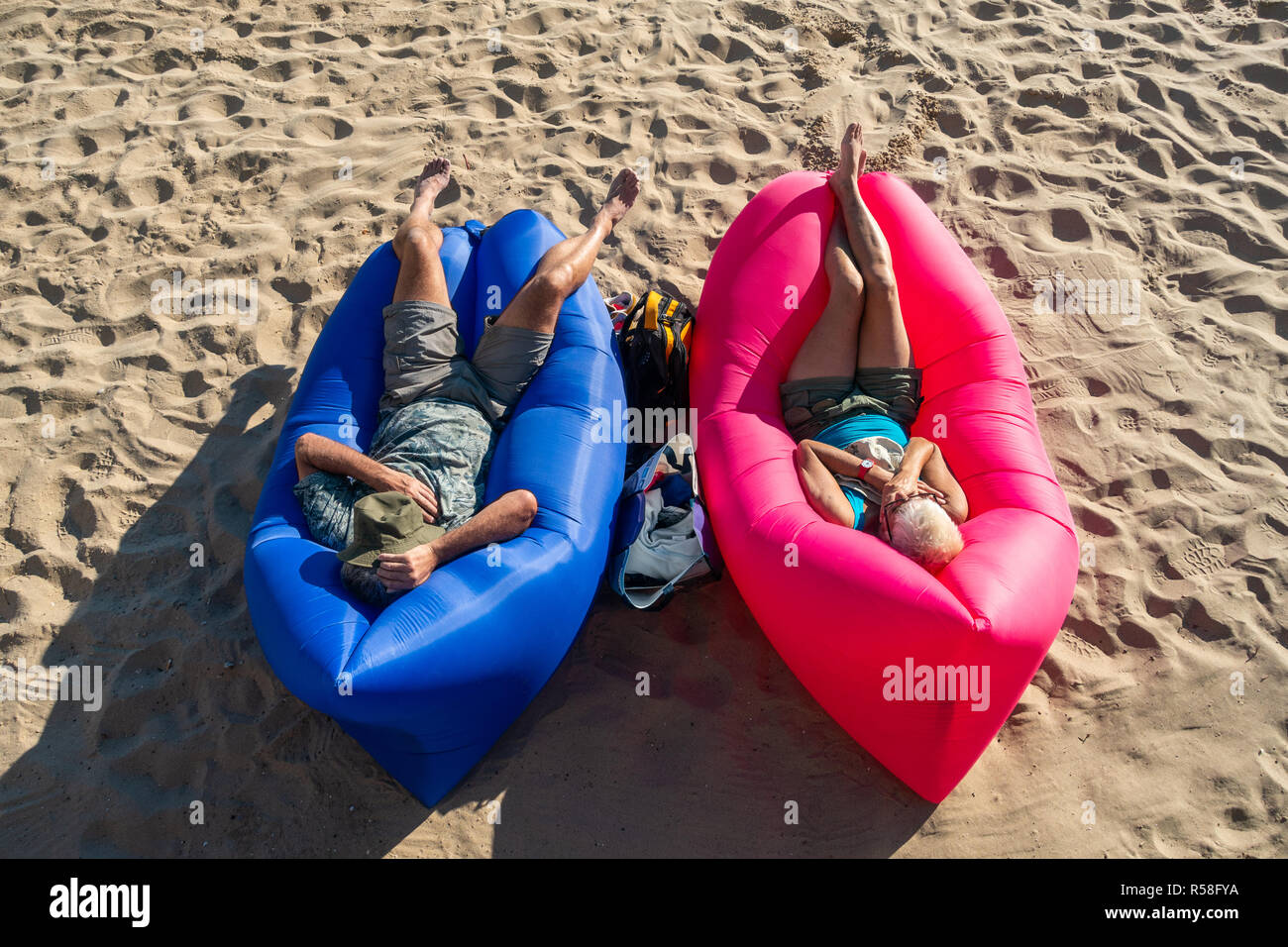 Maschio e femmina di turisti che si siedono sui blu e rosso labbra gonfiabili mobili in spiaggia a prendere il sole su un'aria sdraio sulla spiaggia Foto Stock