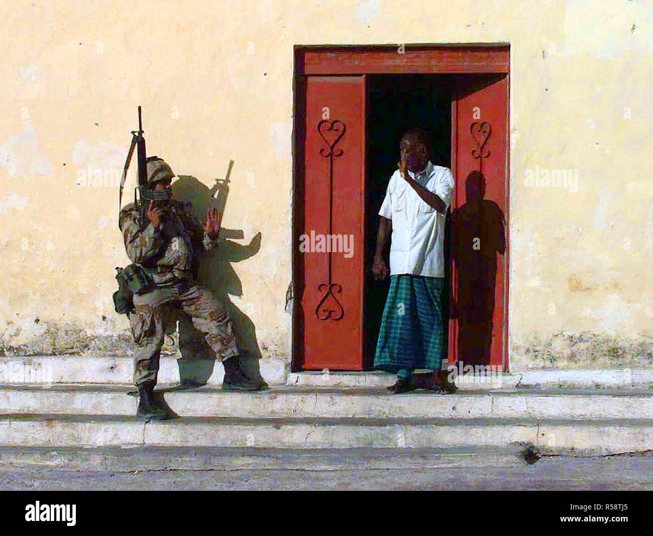 1992 - un marine statunitense e un somalo nervosamente salutarci come l'uomo esce di casa sua per vedere che cosa i Marines stanno facendo. Ripristinare la speranza Foto Stock