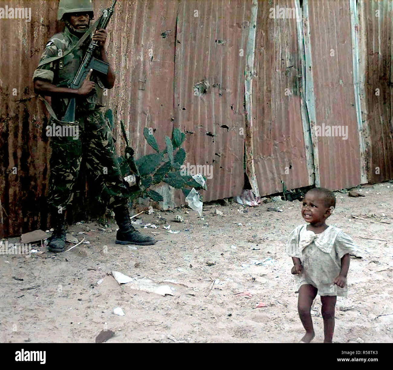 1993 - un pianto toddler somalo passeggiate passato un Botswana Defence Force soldato durante un raid di armi sul mercato Bakara. Il Soldato punti a 7.62mm FN-FAL belga fucile realizzato, nell'aria. Questa missione è a diretto sostegno di Restore Hope. Foto Stock