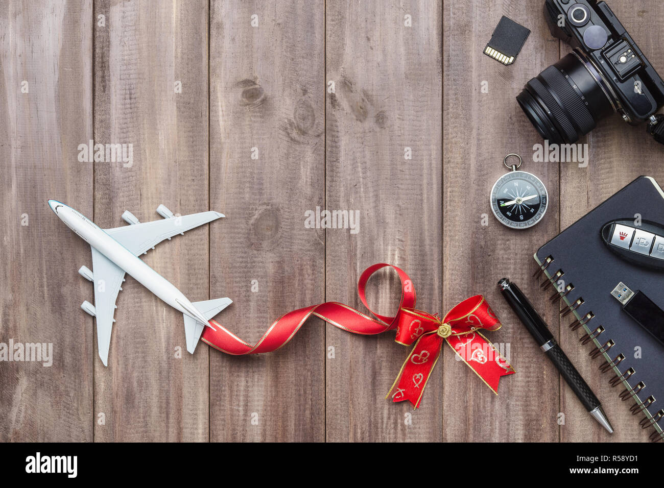 Viaggio Concetto di vacanza. Modello bianco del piano passeggero con cuore archi, fotocamera, scheda SD, unità USB, bussola e notebook su rusty Sfondo legno, parte superiore Foto Stock