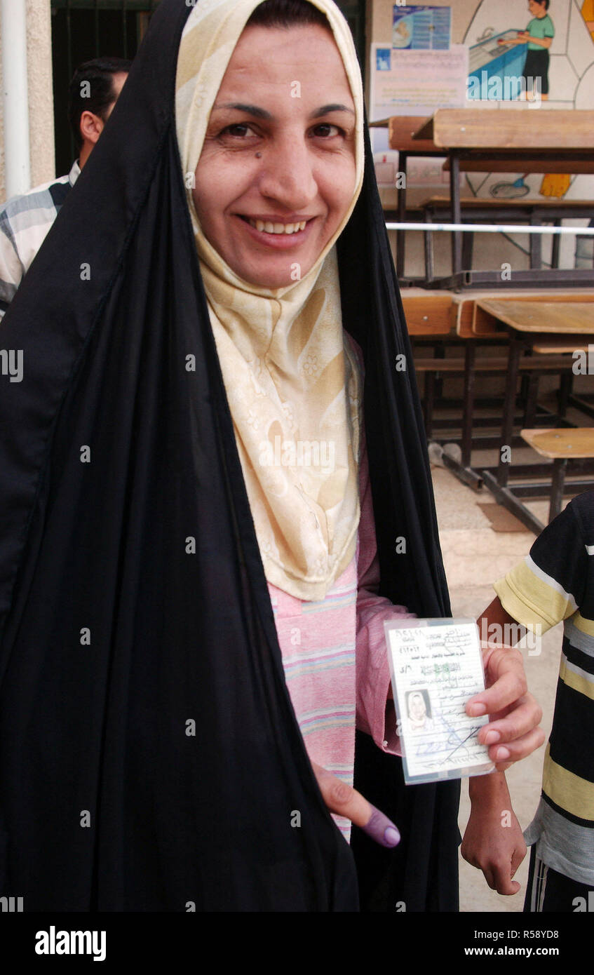 Una donna irachena, vestito in abbigliamento personalizzato, ha il suo dito inchiostrato dopo la colata di una votazione sul referendum costituzionale in corrispondenza di una stazione di polling. Essa visualizza il suo ID utilizzato durante la votazione. Foto Stock