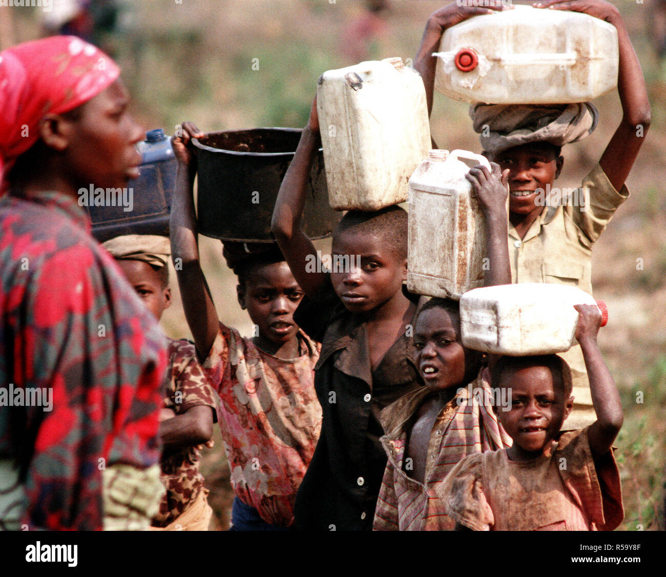 1994 - i bambini sfollati e profughi del Ruanda amaro della guerra civile tra le etnie hutu e tutsi tribù in Africa australe, trasportare contenitori di acqua in cima le loro teste. Foto Stock