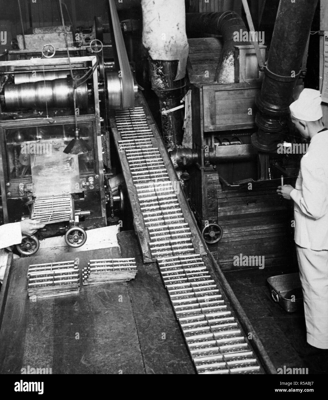 Industrie di guerra - Candy - INDUSTRIE DELLA GUERRA. Rimozione di barrette di cioccolato dalla sagomatura padelle. Tavolette di cioccolato sono riportati i nostri soldati nella parte anteriore come una parte regolare della loro razioni di campo ca. 1918 Foto Stock
