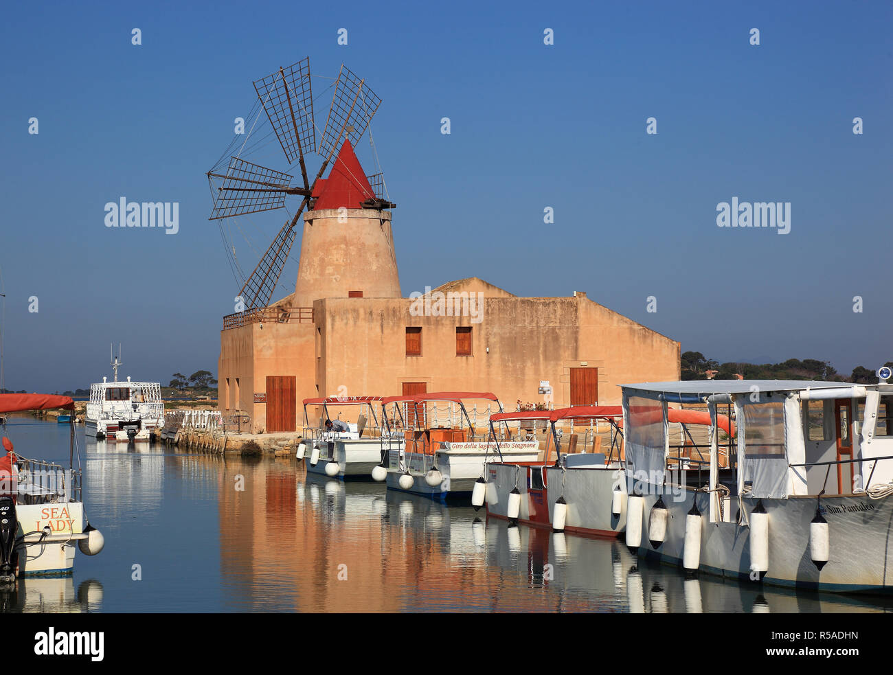 Il mulino a vento e barche presso le saline, nei pressi di Mozia, piccola isola di San Pantaleo off Marsala, Sicilia, Italia Foto Stock