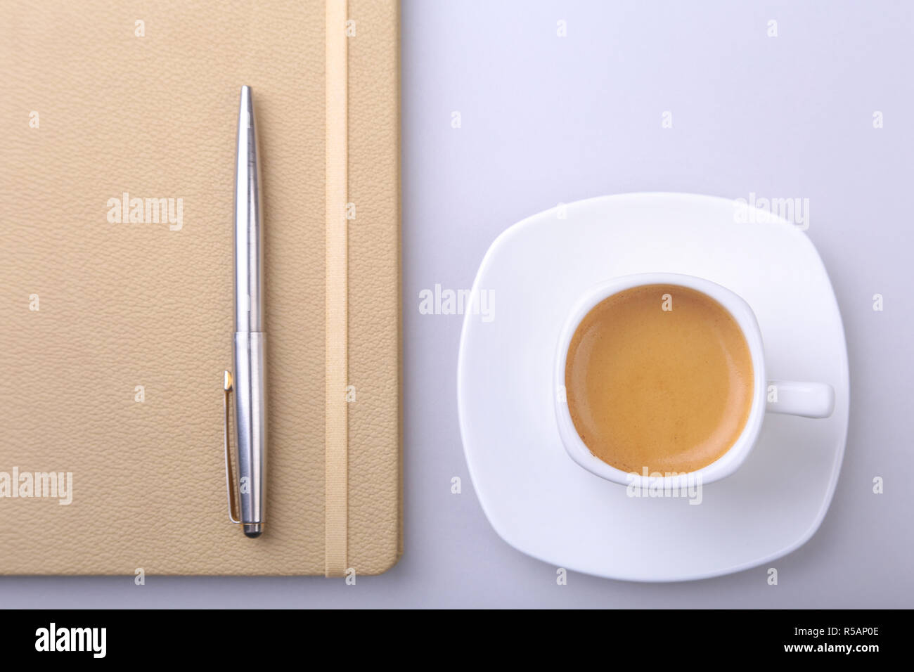 Tazza bianca con un fragrante caffè espresso, notebook elegante e una penna a sfera sulla scrivania in ufficio. Vista superiore Foto Stock