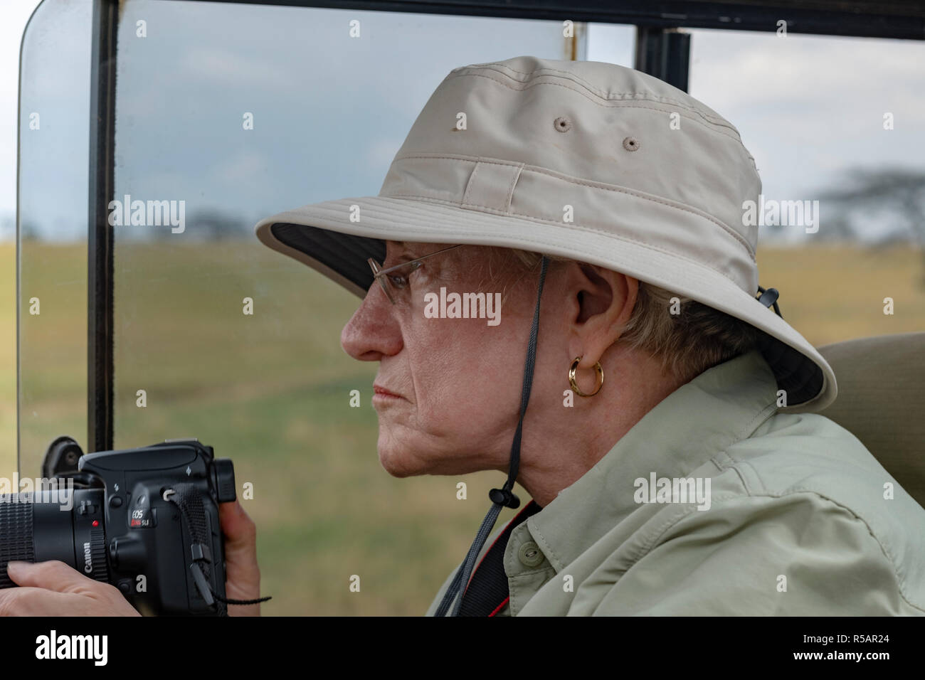 Donna anziana gode di una foto safari in Tanzania da fotografare la natura selvaggia da un Land Rover in Serengetti Parco Nazionale Foto Stock