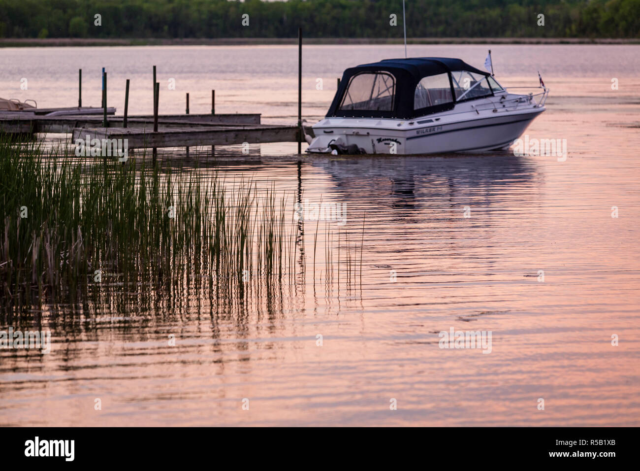 Tranquillo Lago di sunrise, con un piccolo motoscafo legata a un dock. Foto Stock