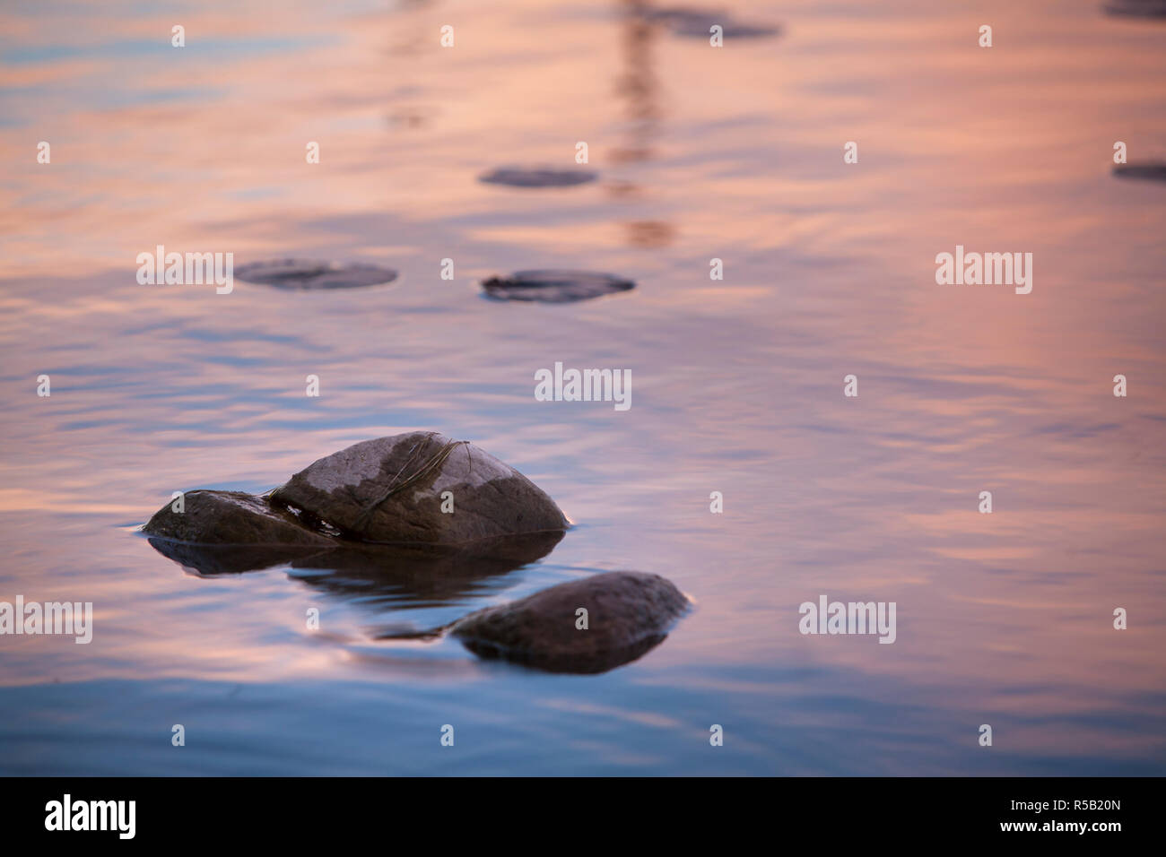La riflessione di un Cielo di tramonto nella superficie del lago con rocce. Foto Stock