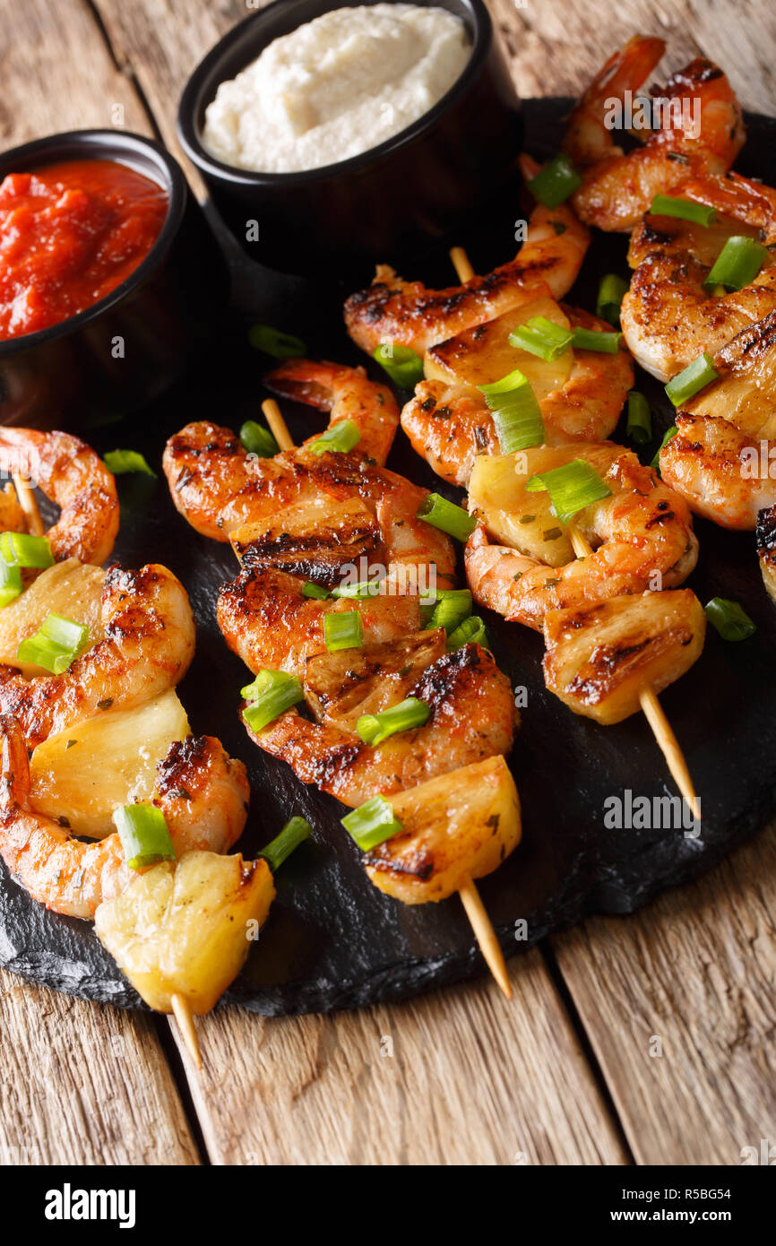 Deliziosi spiedini di gamberi con ananas servite con due salse close-up su una tavola di legno verticale. Foto Stock