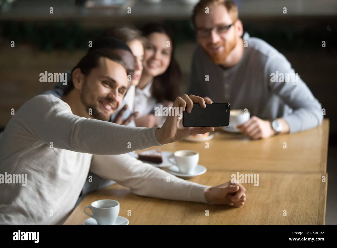 La millenaria guy holding smartphone rendendo Self-portrait immagine a cordiale incontro con i colleghi in cafe, happy amici sorriso per selfie seduta a Foto Stock