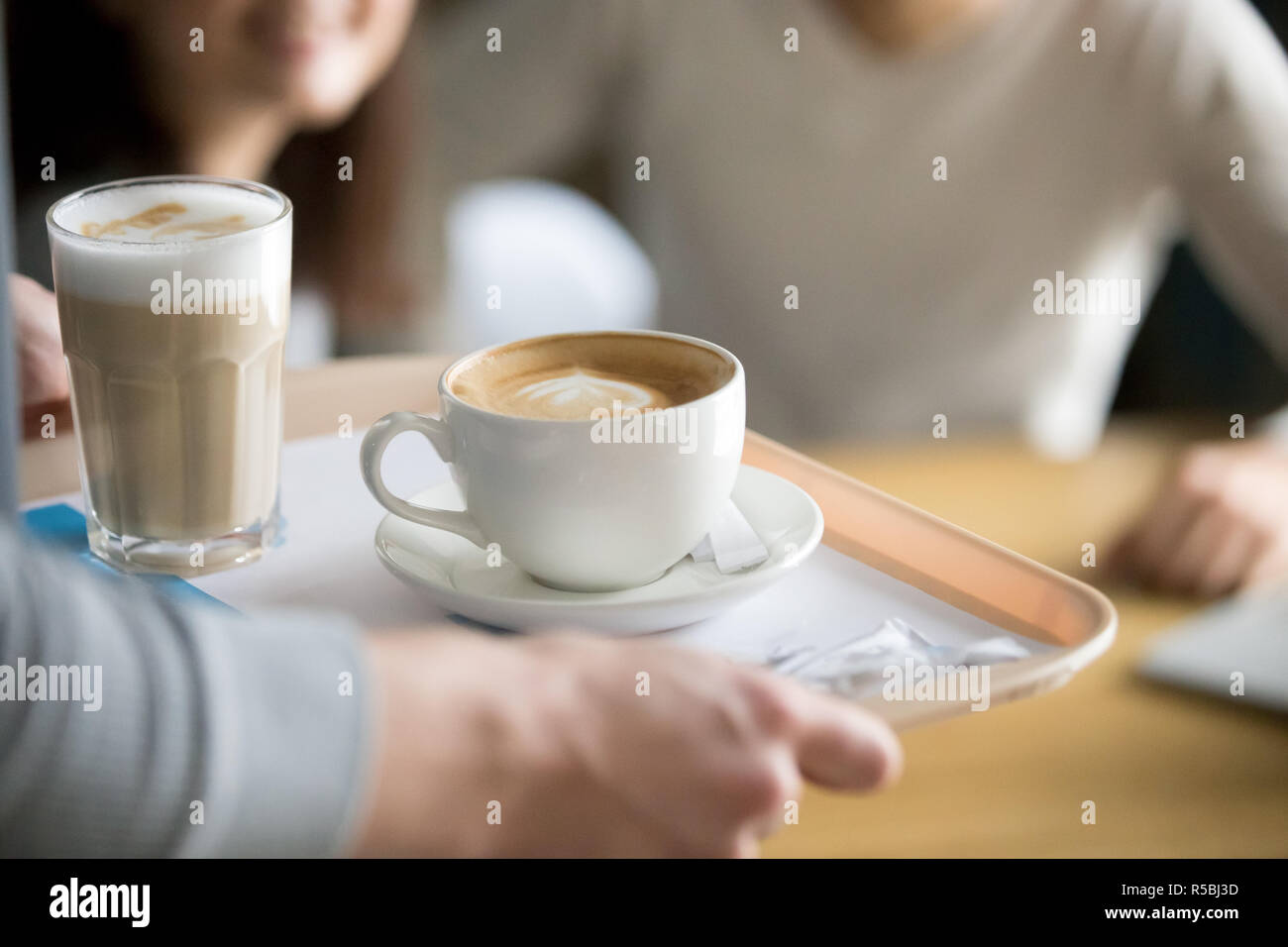 Close up di cameriere aromatico tenuta cappuccino e latte sul vassoio mettere ordine al cafe ospiti, lavoratore coffeeshop dare bevande calde ai visitatori, tazze wi Foto Stock