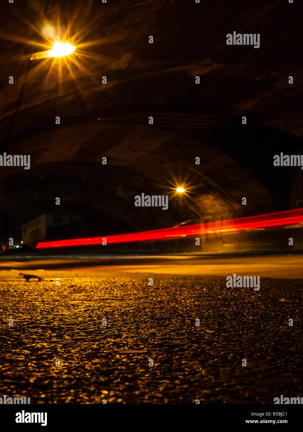 Wet strade della città di notte in un tunnel, con sentieri di luce di una vettura e lampade stradali Foto Stock