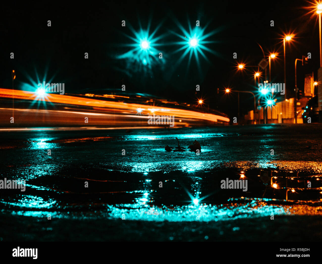 Wet per le strade delle città di notte, con la pozzanghera che riflette le luci, sentieri di luce di una vettura e lampade stradali Foto Stock