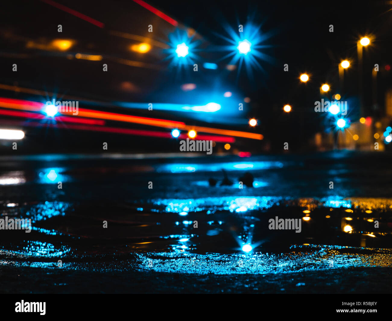 Wet per le strade delle città di notte, con la pozzanghera che riflette le luci, sentieri di luce di una vettura e lampade stradali Foto Stock