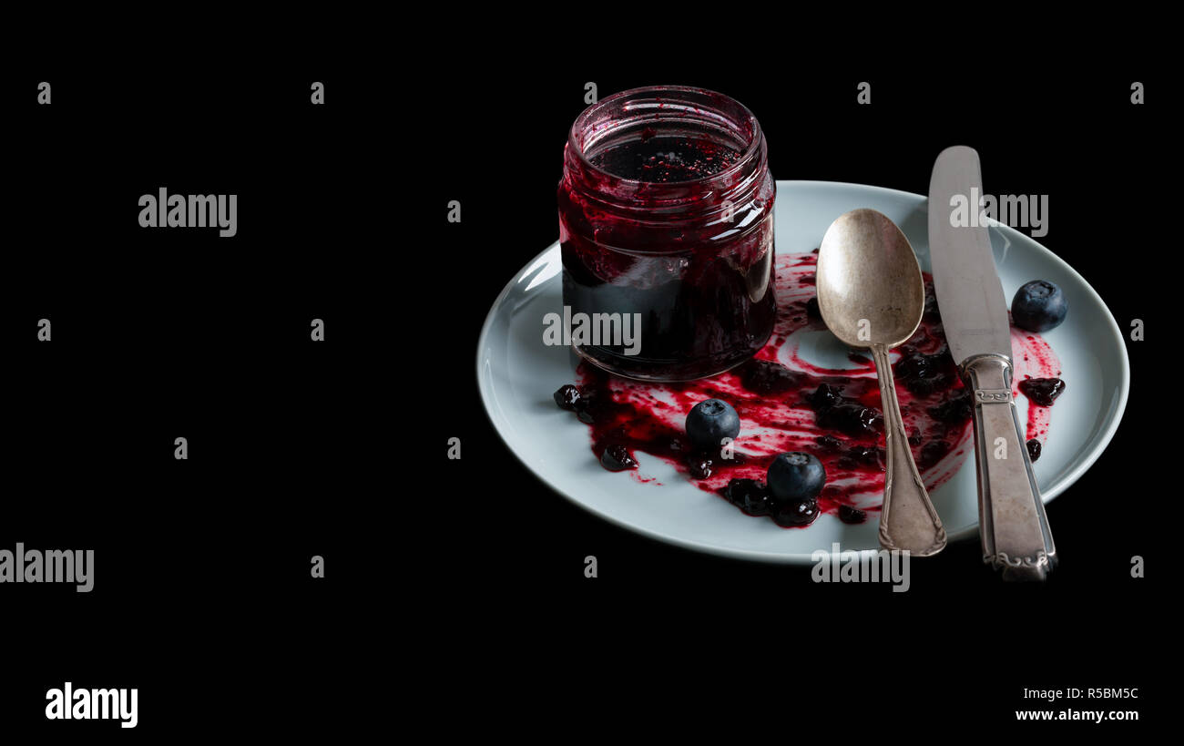 Vasetto di marmellata, un cucchiaio e un coltello su una piastra su uno sfondo nero. Posto per il testo. Foto Stock