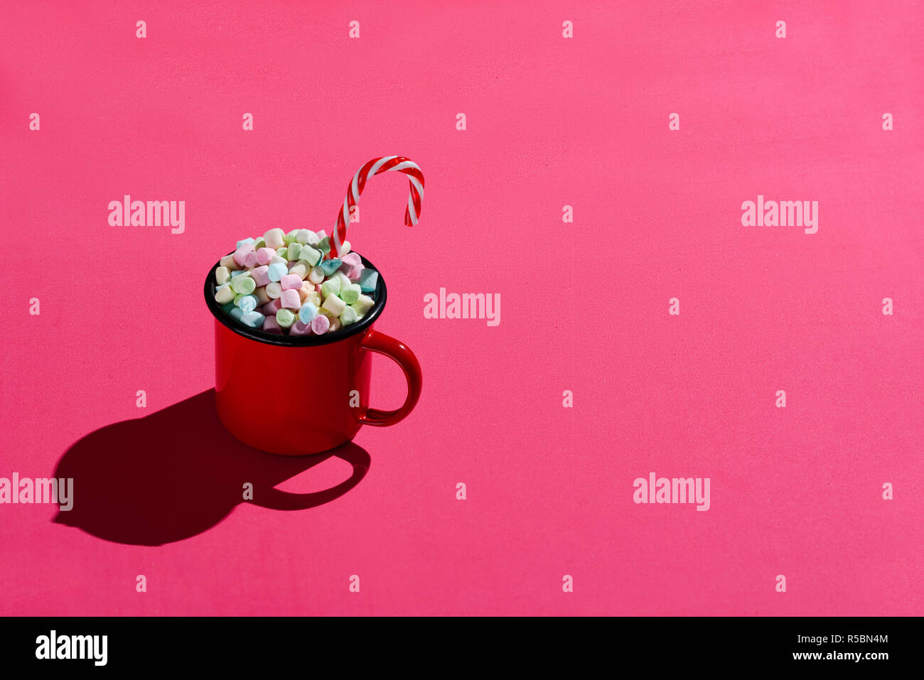 Smalto rosso tazza piena di marshmallows e candy cane su sfondo rosa. Hard Light. Foto Stock