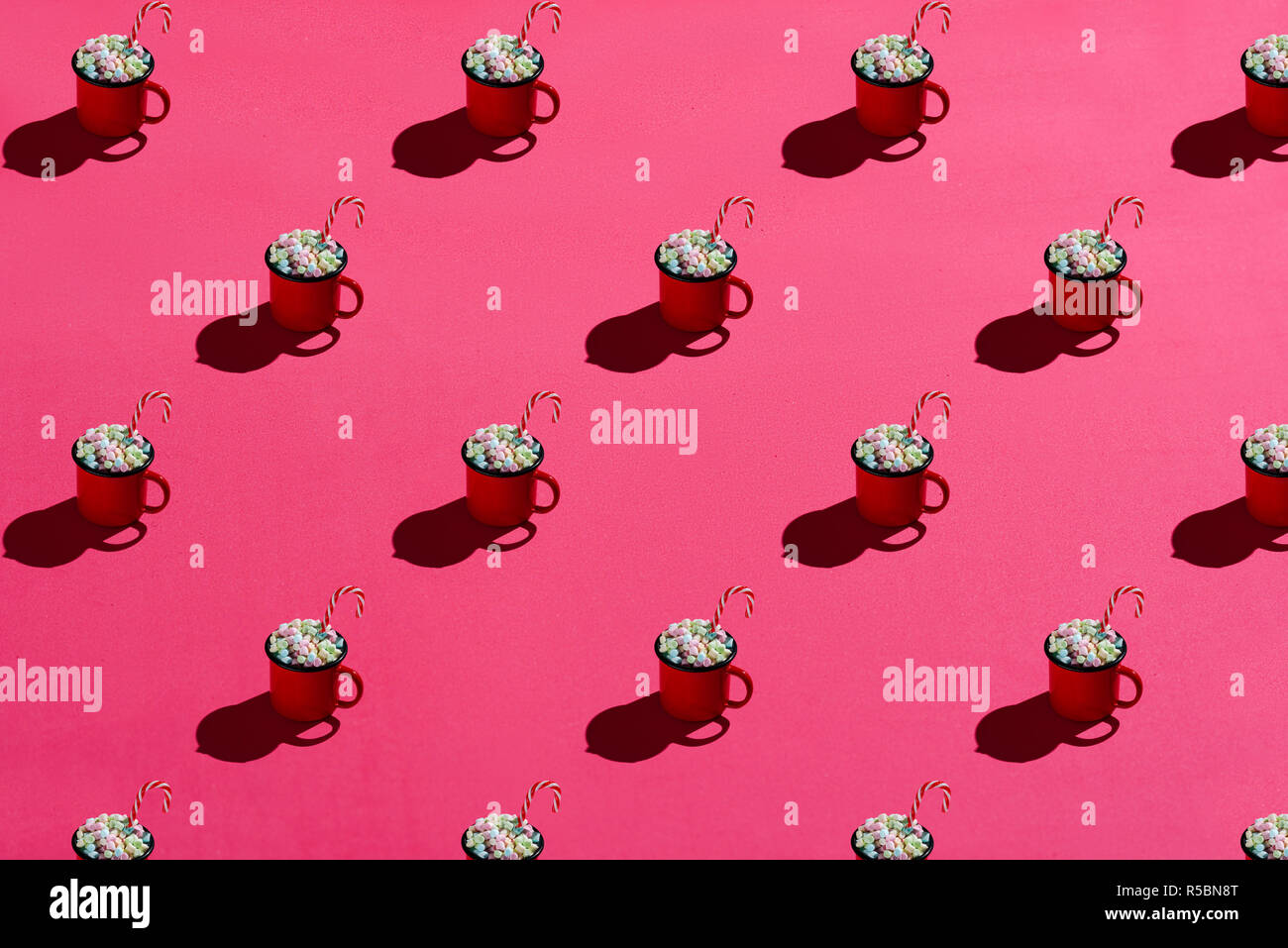 Smalto rosso tazza piena di marshmallows e candy cane su sfondo rosa. Hard Light. Pattern Foto Stock