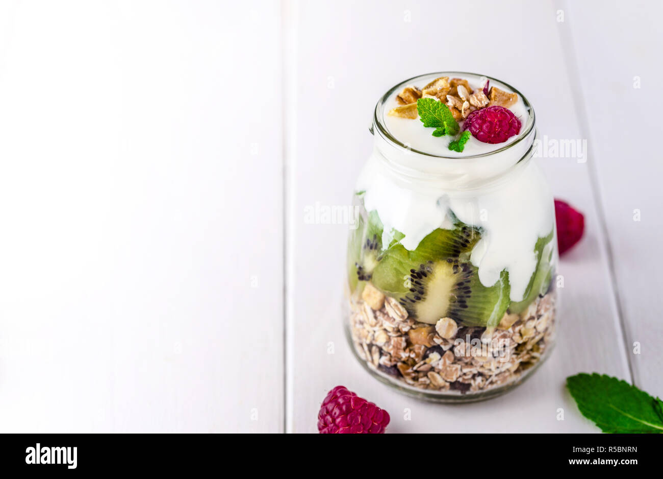 Yogurt bianco con muesli in recipiente di vetro con pezzi di kiwi sulla parte superiore. Foto Stock