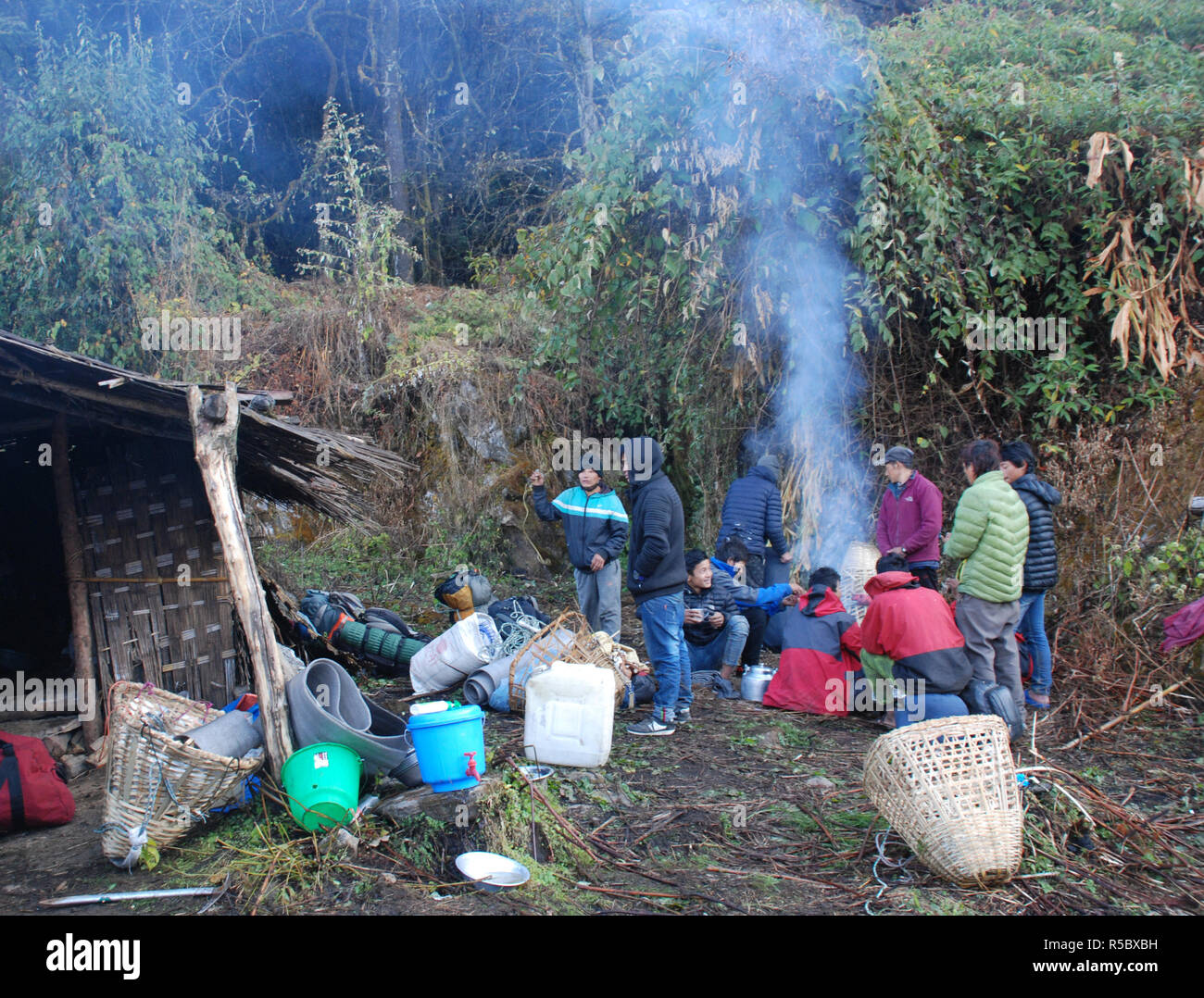Facchini scaldarsi attorno a un fuoco accanto a un piccolo shack nelle foreste del Nepal orientale Foto Stock
